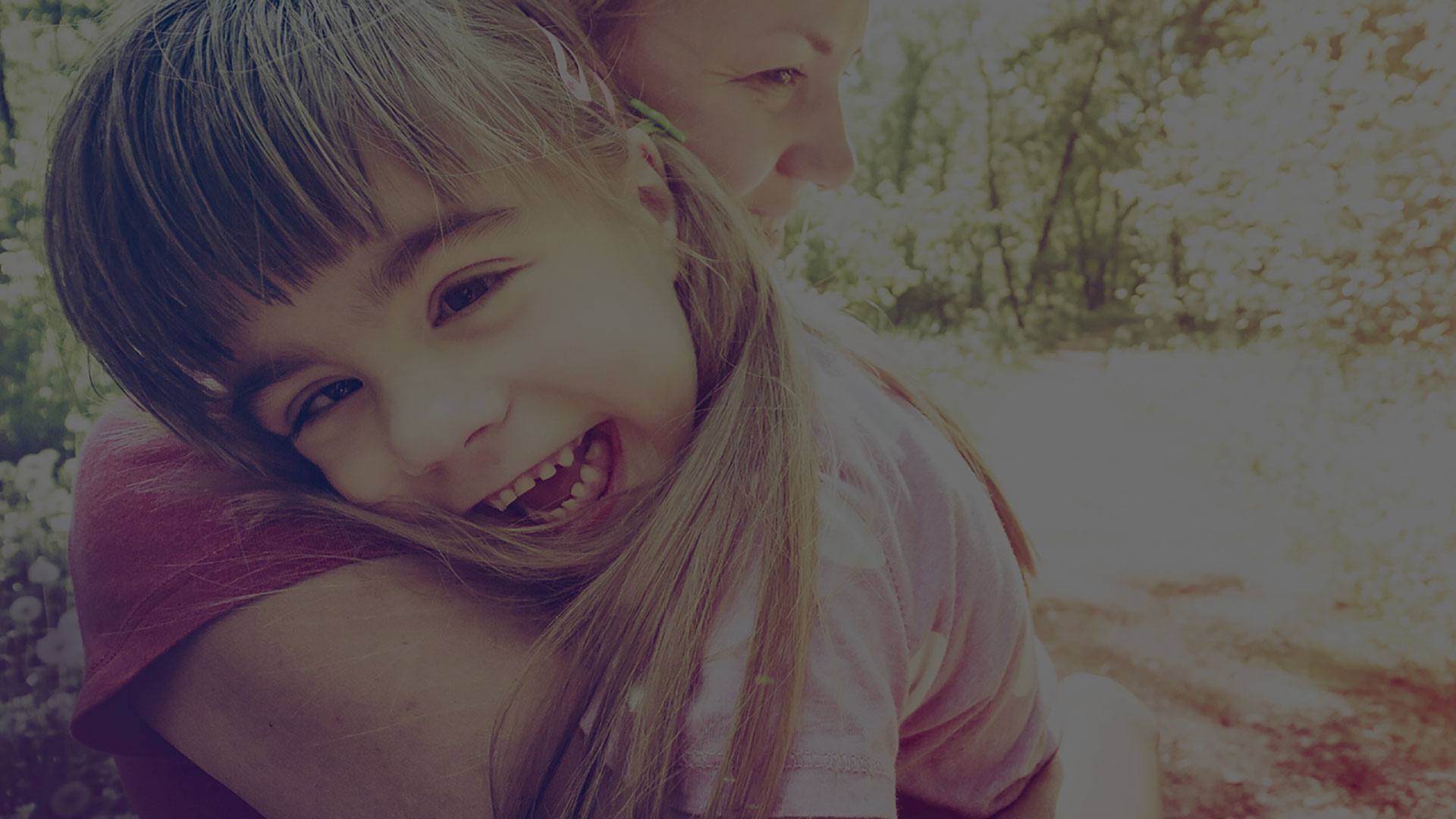 Image of smiling girl being held by her mom
