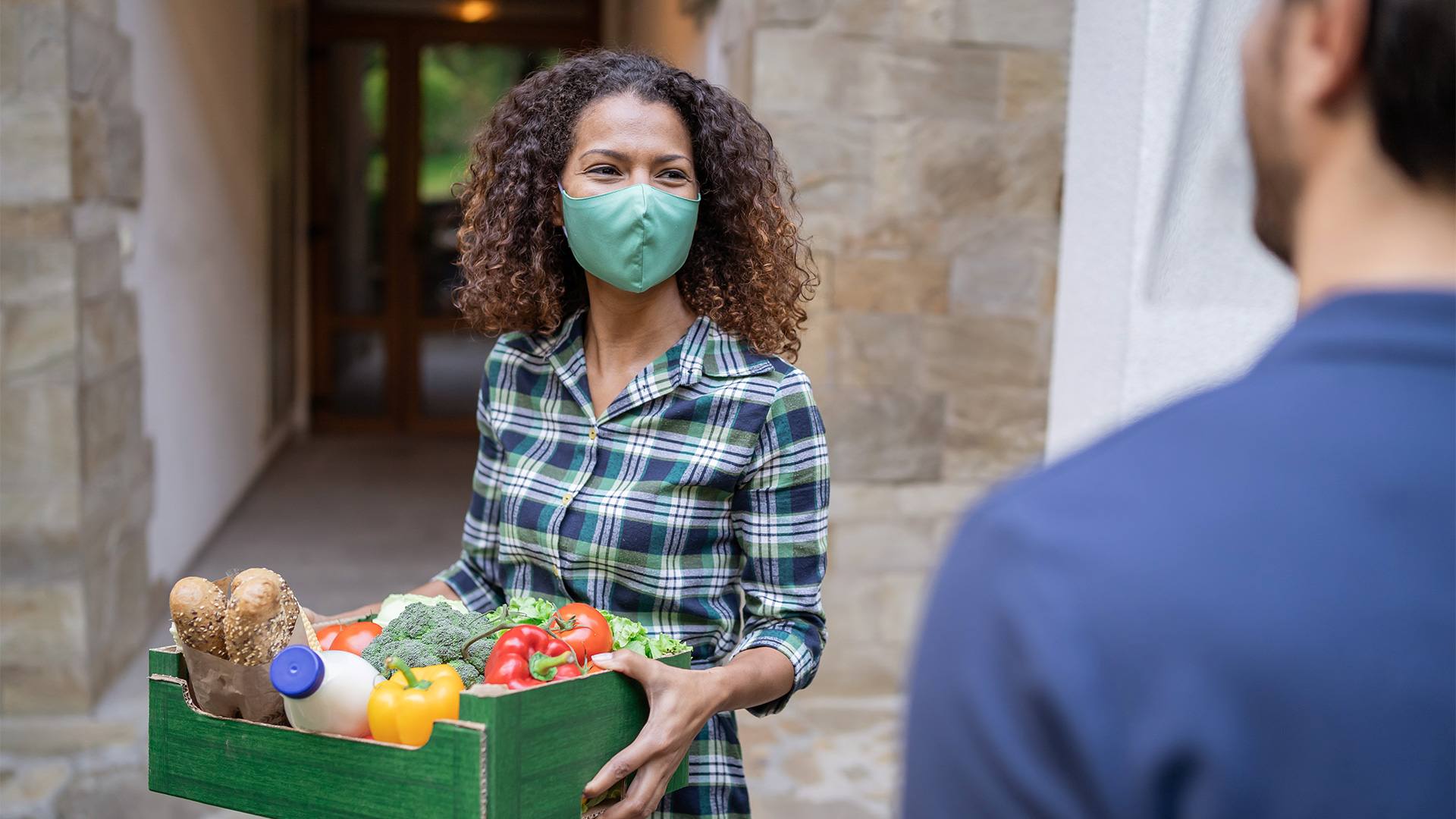 Image of woman holding basket of vegetables wearing a mask
